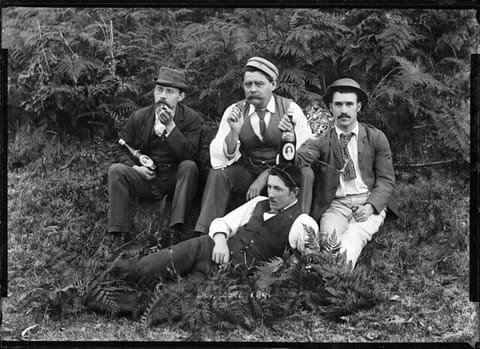 Four well-dressed men holding beer bottles
