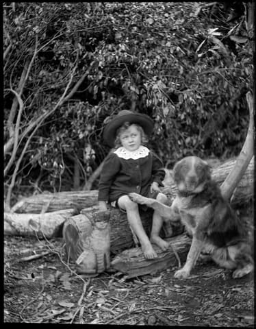 Bare foot boy wearing a hat, seated on a log