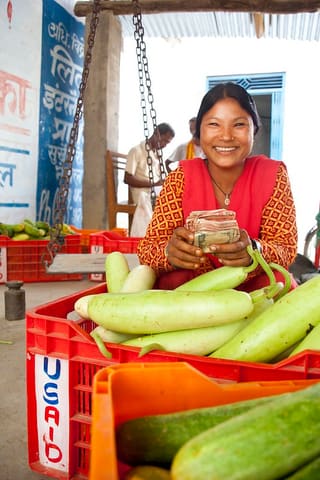 Ram Kumari Tharu displays her harvest and smiles after collecting her money from a local trader. From her fresh cucumber harvest, she earns about Rs. 15,000 every season.