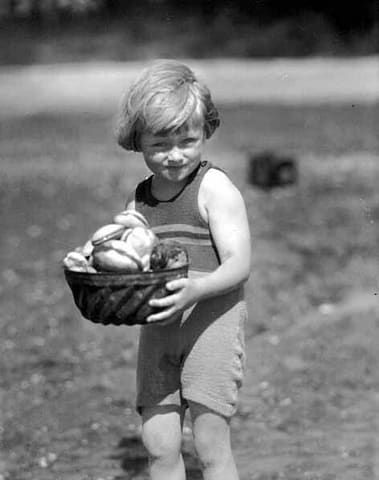 Child in a swimsuit holding a basket of clams, probably Washington State